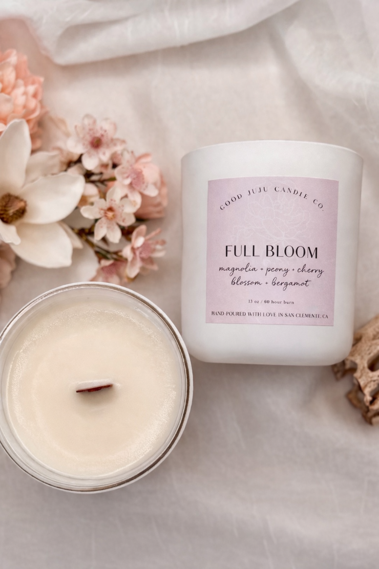 Candle labeled 'Full Bloom' with flowers and a white cloth in the background